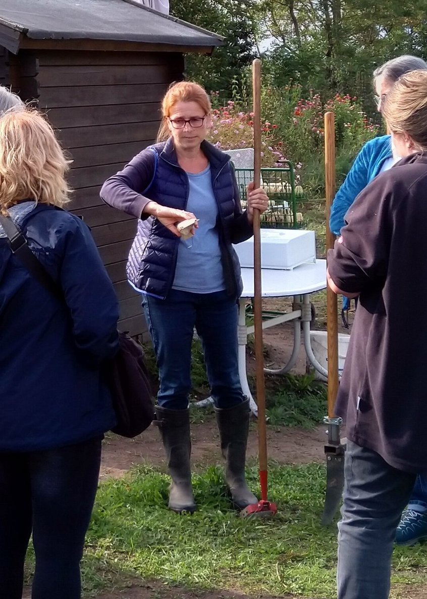 Frau Kummetat-Rottstedt steht mit einem Gartengerät vor einer Menschengruppe und erläutert etwas